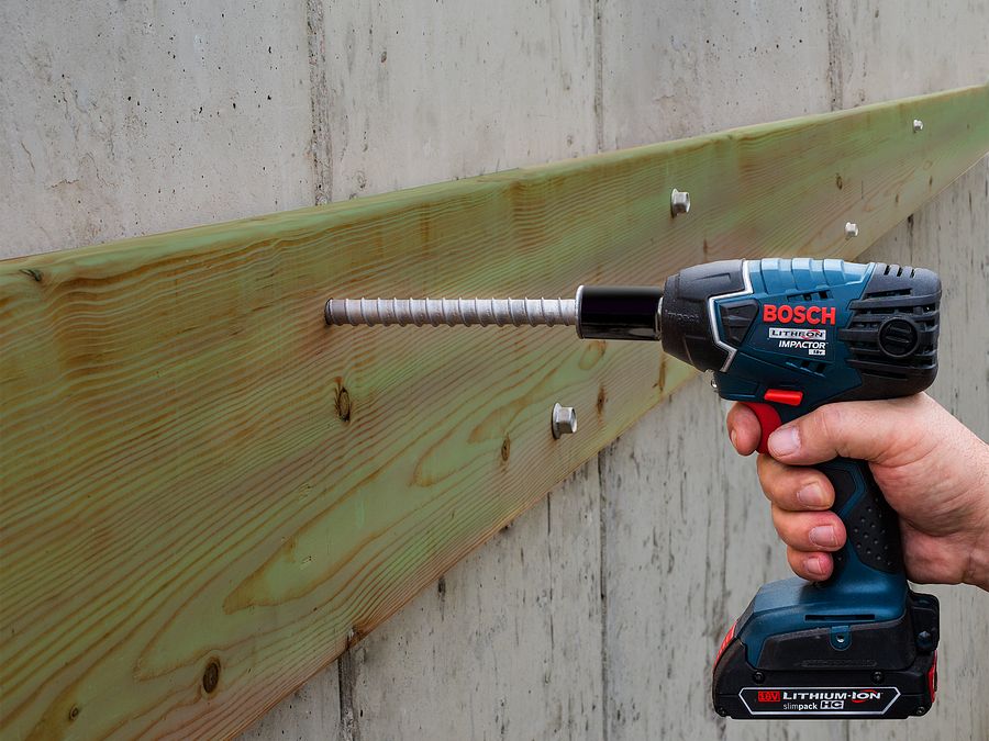 Hand using Bosch drill to drill screw into wood and concrete wall