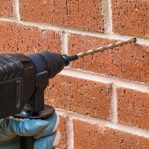 Hand drilling hole into red brick wall