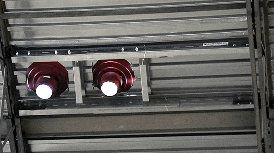 Two red fire sprinkler heads mounted on a metal support frame, secured to the underside of a corrugated steel ceiling.