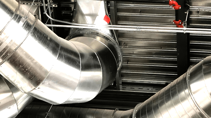 A complex HVAC duct system with large insulated metal pipes running through an industrial ceiling, supported by steel framing.