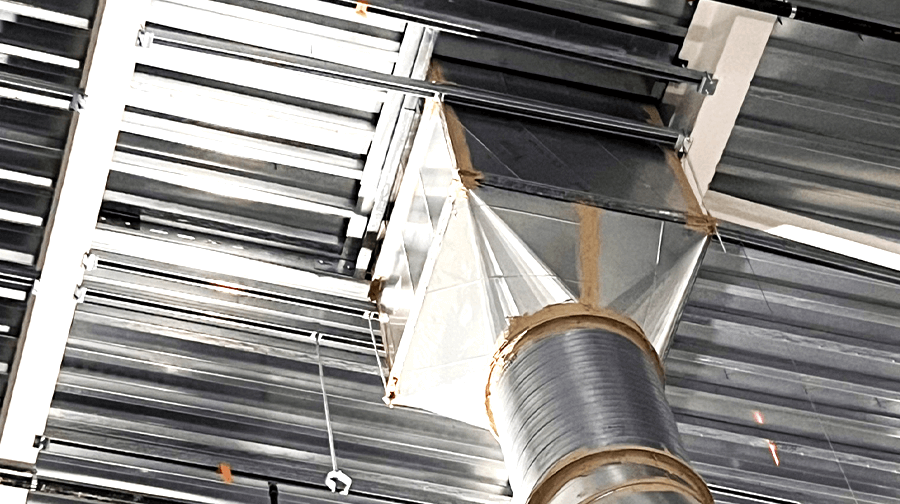 A large HVAC duct system installed within a metal-framed ceiling, supported by steel beams and secured with fasteners.